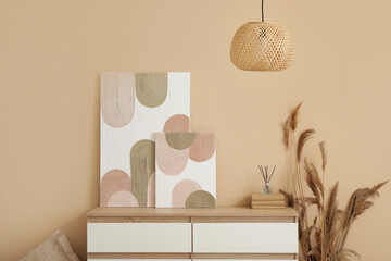 Chest of drawers, pampas grass, lamp and beautiful pictures on beige wall in room