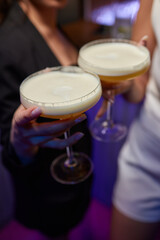 A woman holds a cocktail in her hand, with her fingers wrapped around the glass