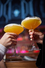 A woman holds a cocktail in her hand, with her fingers wrapped around the glass