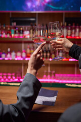 Two friends lifting cocktails in a lively bar scene, expressing joy and celebration
