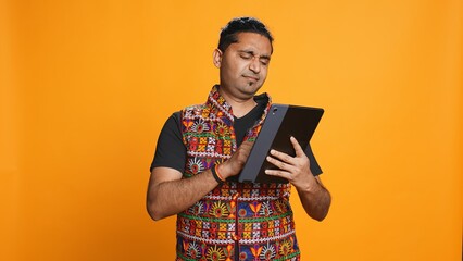 Man upset after lacking necessary money while trying to buy stuff online on tablet. Sad person looking at debit card after getting transaction rejected on device, studio background, camera B