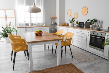 Interior of modern kitchen with white counters, dining table, fruits, chairs and lamp