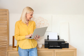 Mature woman using laptop and printer at home