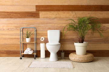 Interior of restroom with toilet bowl, shelving unit and houseplant near wooden wall