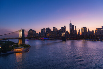 Brooklyn Bridge and New York skyline across the East River under an intense sunset.
