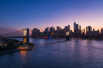 Brooklyn Bridge and New York skyline across the East River under an intense sunset.