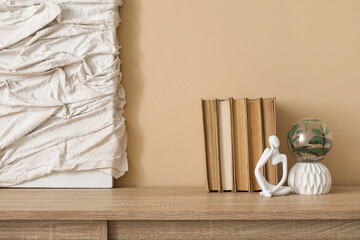 Statuette, picture and books on chest of drawers near beige wall in stylish room, closeup