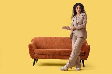 Obraz premium Young African-American businesswoman pointing at red sofa on yellow background