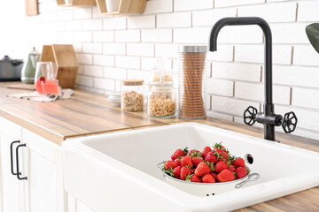 Colander with tasty strawberries in kitchen sink