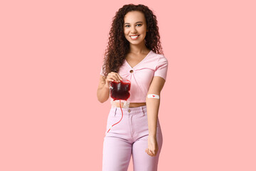 Young female African-American donor with applied medical patch and blood pack on pink background