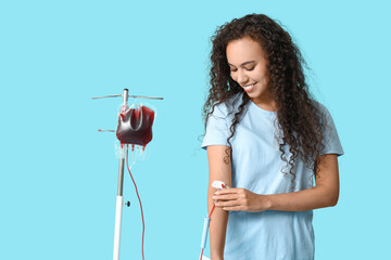 Young female African-American donor with applied medical patch donating blood on blue background
