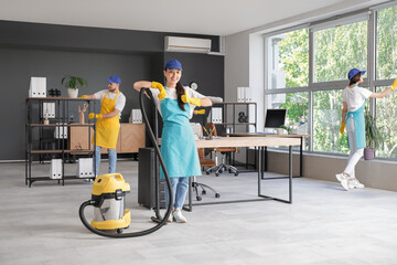 Female Asian janitor with vacuum cleaner showing thumb-up in office