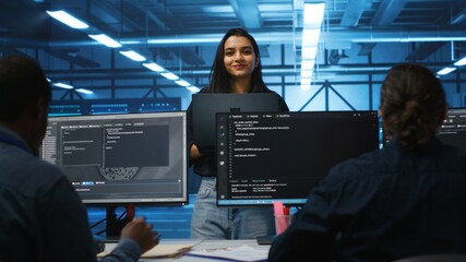 Portrait of smiling Indian manager in server room managing team of engineers looking for equipment...