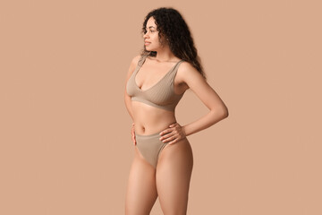 Beautiful young happy African-American woman in underwear on beige background