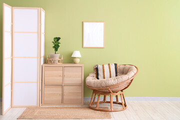 Interior of room with folding screen, commode and armchair near green wall