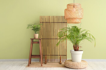 Interior of room with wooden folding screen, chair and houseplants near green wall