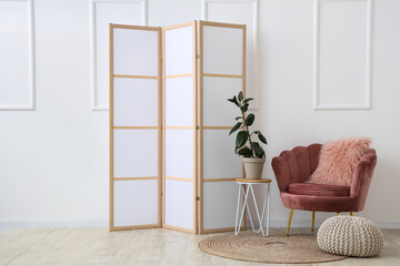 Interior of room with folding screen, houseplant and armchair near white wall