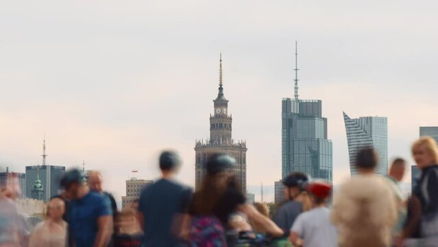 Time-lapse unrecognizable people crowd walking on pedestrian bridge over river in Warsaw city, Poland. Lot of people crossing street, blurry pedestrians on summer day. Downtown skyscrapers on horizon