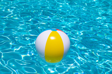 Beach ball floating in swimming pool. Advertising for summer vacations. Space for text. Colorful beach ball in swimming pool.