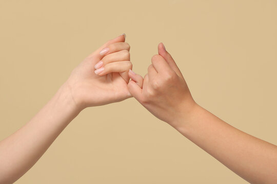 Women making pinky promise on color background, closeup. Friendship Day celebration
