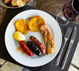 Appetizing grilled chorizo, botifarra and morcilla sausages, slice of bacon and breaded eggplants...