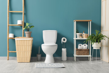Interior of restroom with toilet bowl, bin, ladder and shelving unit near blue wall