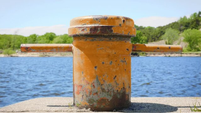 Chipped orange metal boat cleat on edge of marina