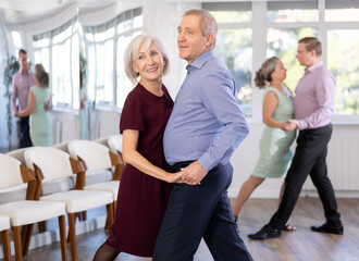With unhurried music, elderly couple spins to rhythm of tango during lesson for novice students....