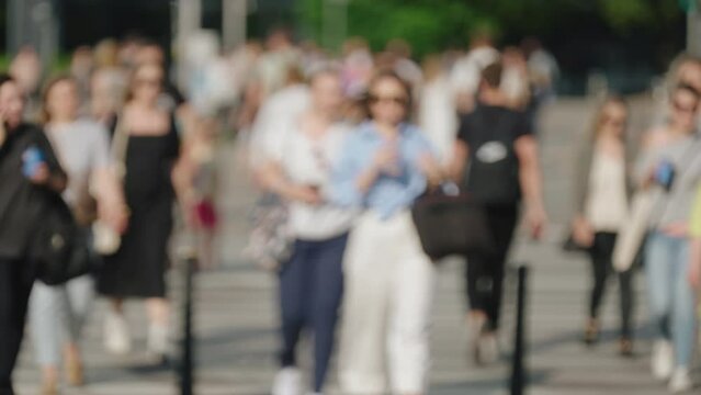 Bokeh blurred people crowd walking crossing busy street slow motion, city life, lot of pedestrians crowded crosswalk, rush hour intersection sidewalk on sunny summer day. Blurry cityscape background
