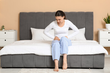 Young woman suffering from cystitis on bed at home