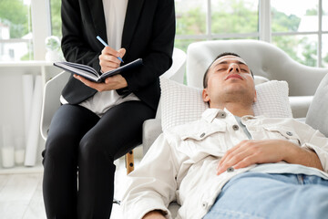 Female psychologist writing on notebook with hypnotized patient in office