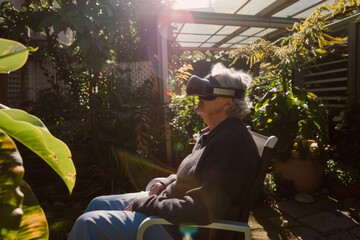 An elderly woman wearing a virtual reality headset sits in a sunlit garden, exploring new technology. Senior Woman Experiencing Virtual Reality in Garden