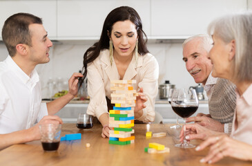 Happy mature and young family members sitting at table with a glass of wine while playing with...