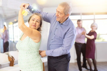 Senior man and elderly woman are dancing classic version of waltz in couple during lesson at studio. Leisure activities and physical activity for positive people.
