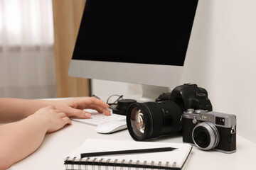 Photographer working on computer at white table with cameras indoors, closeup