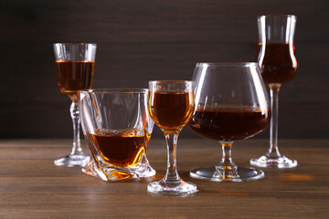 Different delicious liqueurs in glasses on wooden table