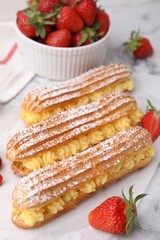 Delicious eclairs filled with cream and strawberries on table