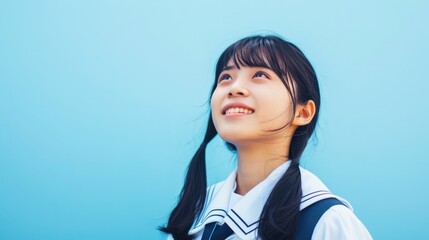 Portrait of a beautiful smiling Japanese high school girl wearing a sailor uniform, looking up at the sky with a blue background