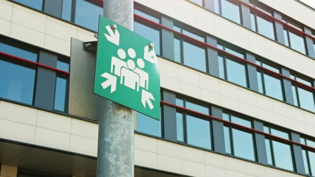A safety sign indicating the emergency assembly point outside a modern office building for precautionary measures and evacuation procedures
