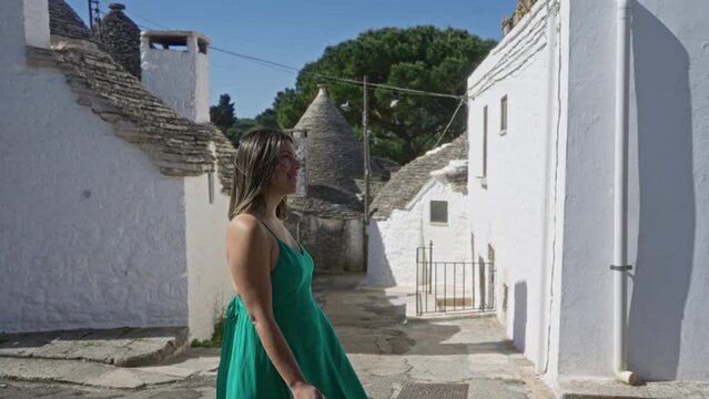 A young hispanic woman walks through the picturesque streets of alberobello, italy, surrounded by traditional white trulli houses on a sunny day.