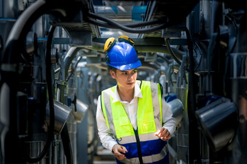 A focused engineer wearing a safety vest and helmet inspects machinery in an industrial setting. The professional diligently checks equipment to ensure proper functionality and safety standards.