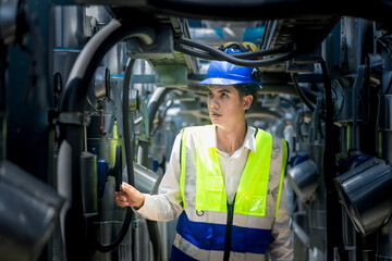 A focused engineer wearing a safety vest and helmet inspects machinery in an industrial setting. The professional diligently checks equipment to ensure proper functionality and safety standards.