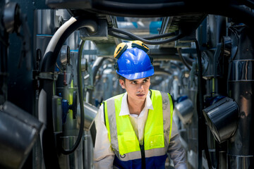 An industrial worker in high-visibility gear and a blue helmet meticulously examines the intricate...