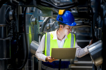 An industrial worker in high-visibility gear and a blue helmet meticulously examines the intricate network of machinery. The engineer is dedicated to maintaining operational efficiency and safety.