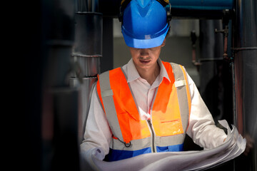 An industrial worker in high-visibility gear and a blue helmet meticulously examines the intricate...