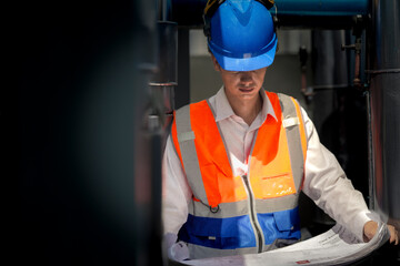 An industrial worker in high-visibility gear and a blue helmet meticulously examines the intricate...