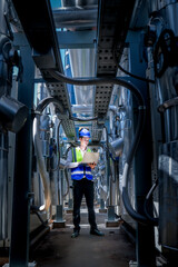 An industrial worker in high-visibility gear and a blue helmet meticulously examines the intricate...