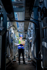 An industrial worker in high-visibility gear and a blue helmet meticulously examines the intricate...