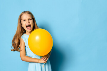 Joyful little girl in blue dress holding a bright yellow balloon against a matching blue background