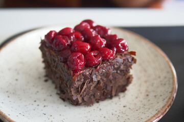 Delicious chocolate cake slice with cherry topping on white plate in a closeup photo